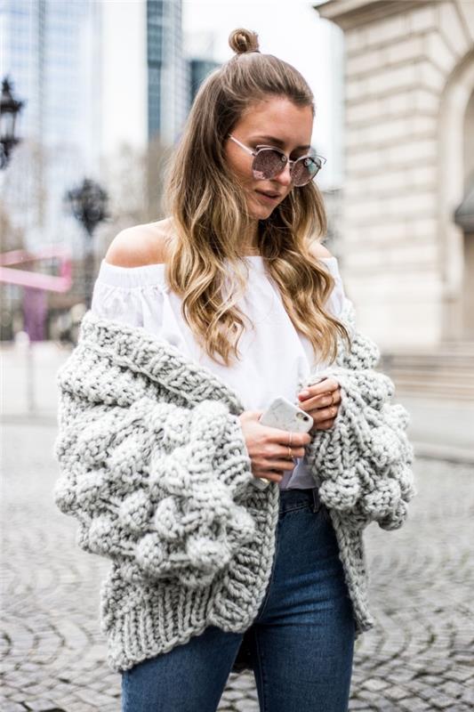 idėja, kaip dėvėti didelį moterišką megztinį megztiniu su balta palaidine nuo peties ir tamsiais džinsais