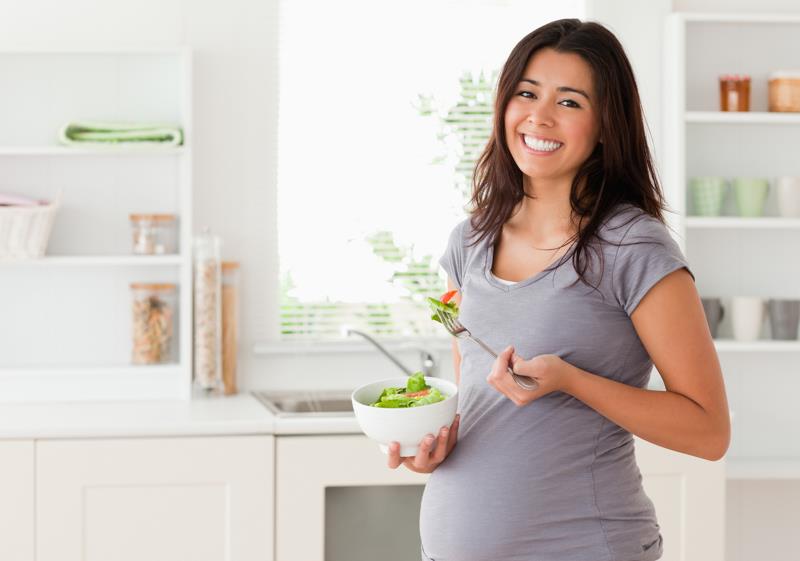 patraukli nėščia moteris stovi laikydama dubenį salotų