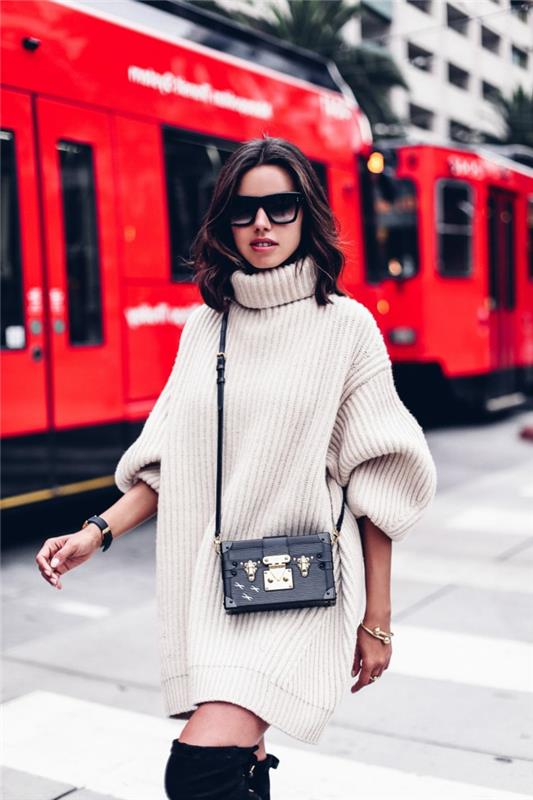 šiuolaikiška moteris, dėvi kreminį megztinį, mažą juodą krepšį, akinius nuo saulės, aukštakulnius batus šlaunyje, storą megztinį