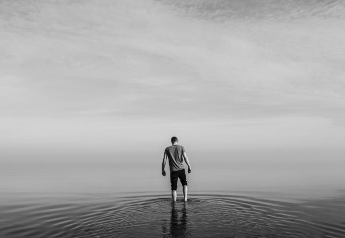 črno -beli portret mladeniča bosa v mirni morski vodi, v ozadju obzorje, skrito v megli