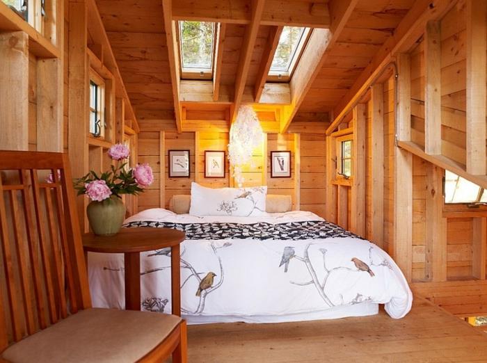 yazlık tarzı iç mekan, çatı altında yatak, ahşap ve tekstil koltuk, çiçekli vazo, pencerenin altında yatak