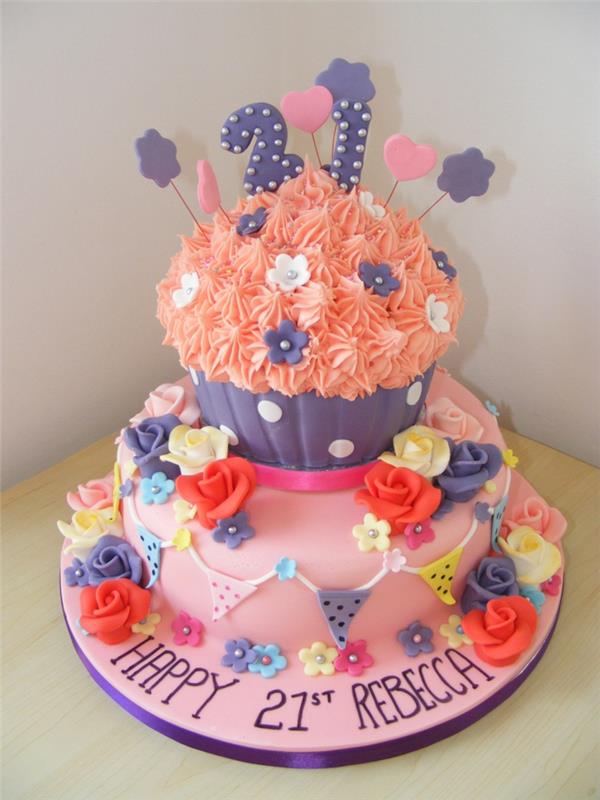 rožinės ir oranžinės spalvos tortas, keksiukų skulptūra ant torto, užrašai ir valgomos gėlės