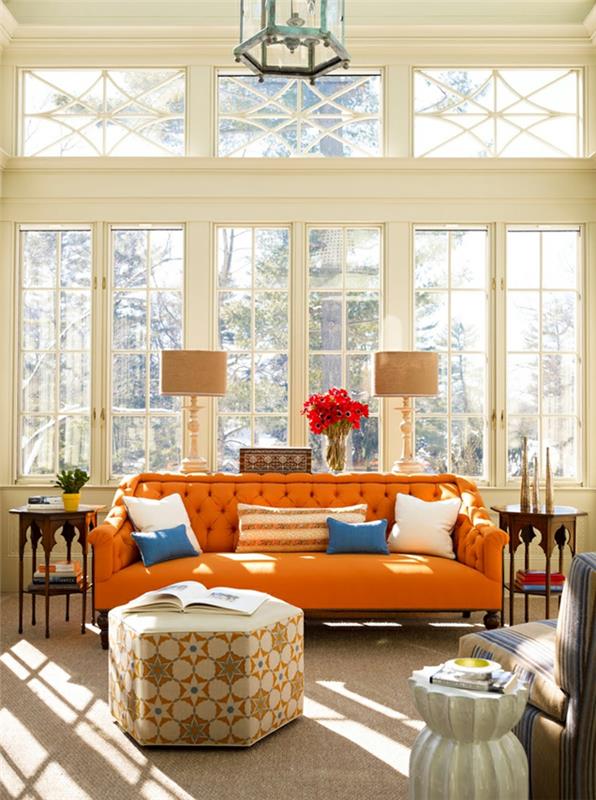 oranžinė minkšta sofa, smėlio spalvos pufas, smėlio spalvos stalinės lempos, didelis langas, žibinto lubų šviestuvas