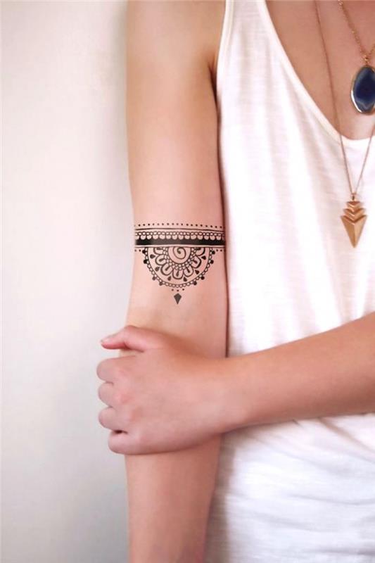ženska tetovaža s kano, ženska roka za tetoviranje, dva obeska in subtilne ogrlice, bela brezrokavnica
