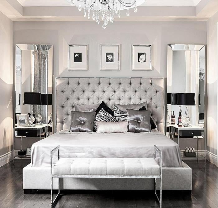 krištolinė liustra, pilka kuokštinė galvūgalis, dekoratyvinės pagalvėlės ant lovos, juodos lempos