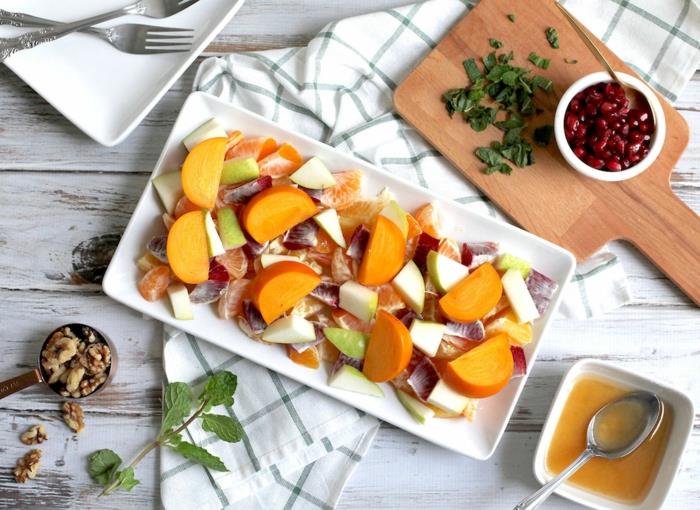 žiemos patiekalas, patiekiamas ant stačiakampės baltos lėkštės, medinės lentos, sirupas vaisių salotoms, graikiniai riešutai