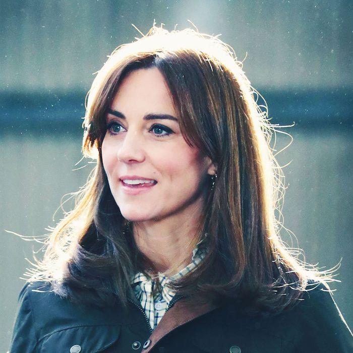 Kate Middleton, ekose bir bluz giymiş, perde kaküllü bir saç modeli takıyor.