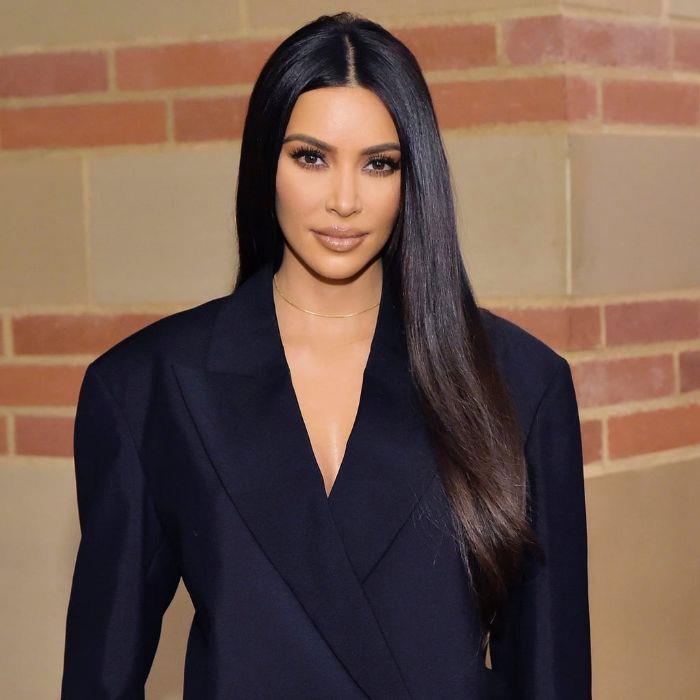 kim kardashian labai ilgais ir glotniais tamsiai rudais plaukais, išsiskiriančiais galvos viduryje