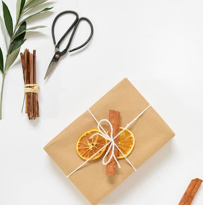 kraftinis dovanų popierius, papuoštas balta virvele, džiovintomis apelsinų skiltelėmis ir cinamonu, paprasta ir originali idėja