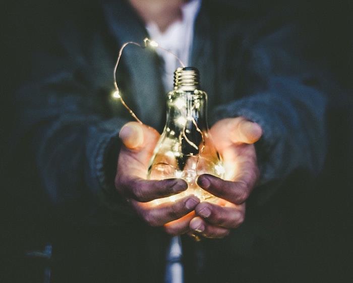 Vyrų rankų nuotrauka su LED lempute, tiesiog keičiantis energijos tiekėjas