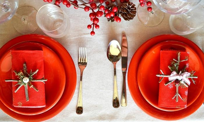 raudonos lėkštės ant baltos staltiesės, elegantiški indai, raudonos uogos, sulankstytos ir sandarios servetėlės ​​su snaigėmis pagaliukuose