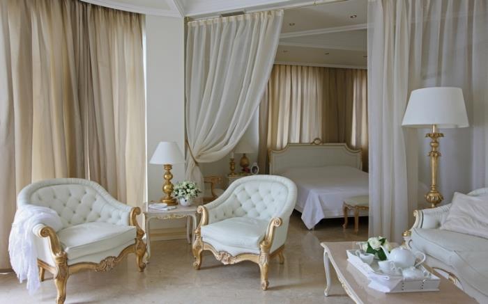 beyaz ve altın mobilyalarla retro barok tarzda döşenmiş yatak odasında uzun ekru perdeler