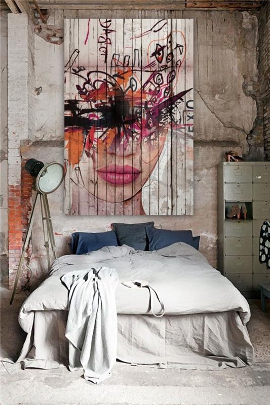 modernus, pramoniniu stiliumi įrengtas miegamasis su neapdoroto dizaino grindų lempa ir sienų dailės gobeleno apdaila