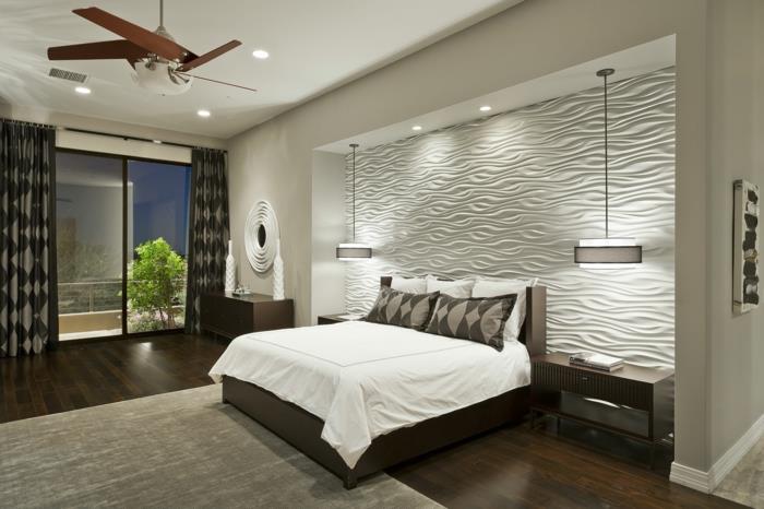 baltas miegamojo sienų dekoras, smėlio spalvos kilimas, medinės grindys, ventiliatoriaus lempa, erdvus miegamasis