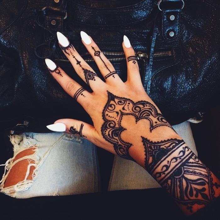 velika tetovaža s kano, beli nohti na stiletto, tetovaže z majhnimi prsti, roka na črni usnjeni torbici