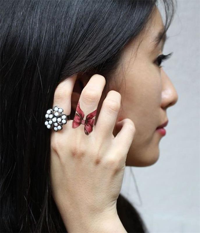 ženska, ki drži črne lase, beli biserni prstan, rdeč lok, tetovaža s srednjim prstom, tetovaže prstov za ženske