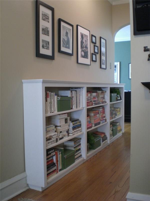 velika bela omara s policami s knjigami in škatlami, nad njo visi več fotografij v različnih velikostih in barvnih okvirjih, ideje za okrasitev hodnika, lesena laminatna tla