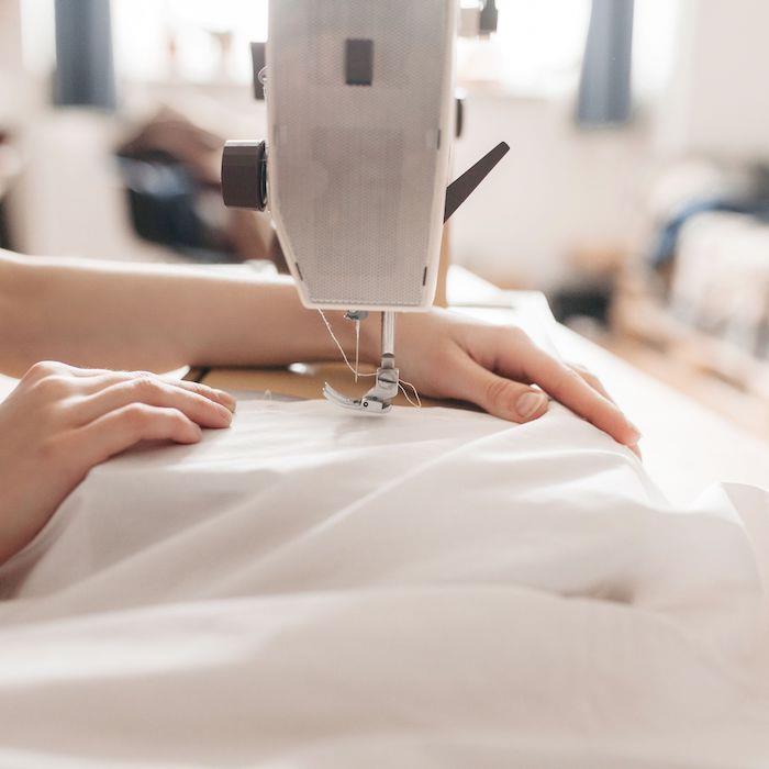 postopek šivanja tkanine z žensko roko in stroj za šivanje bele tkanine