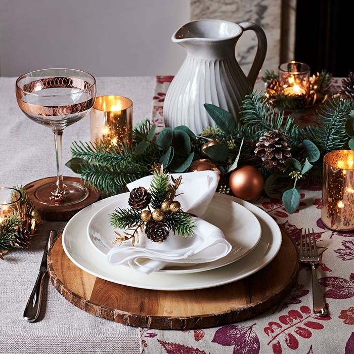 najlepše božične mize lesena podložka bela plošča prtiček zelenje borovi storžki kozarci rožnato zlati poudarki