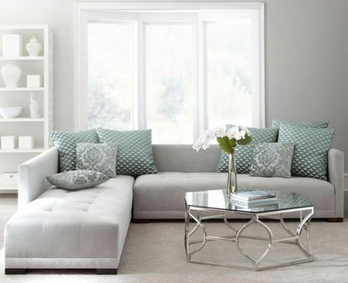 šviesiai pilka kampinė sofa, turkio spalvos mestos pagalvės, pilkos miegamojo sienos, stiklinis kavos staliukas