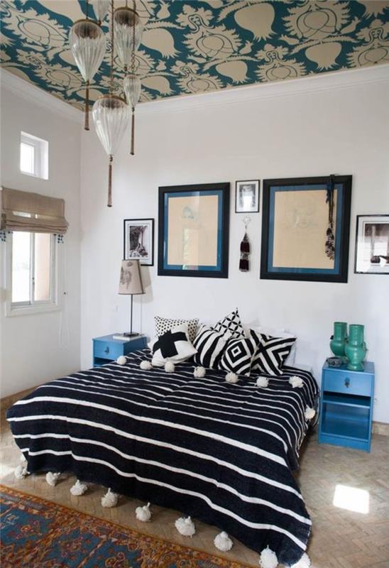 Fas dekor aksanlarına sahip etnik şık bir yatak odası, geometrik desenli minderlerle ilişkili ponponlu Fas çizgili battaniye