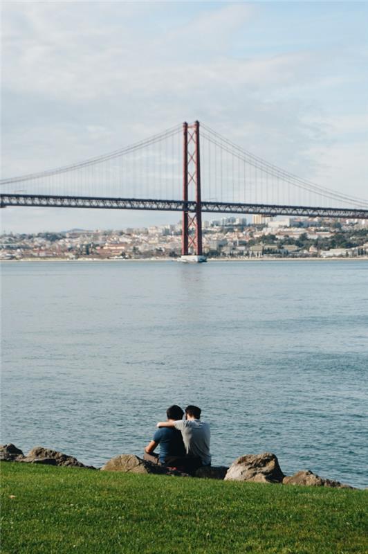 Çimenlikte romantik çift ve Lizbon'daki kırmızı köprünün takdire şayan manzarası, romantik çift, aşık görüntü çifti güzel romantik fotoğraflar