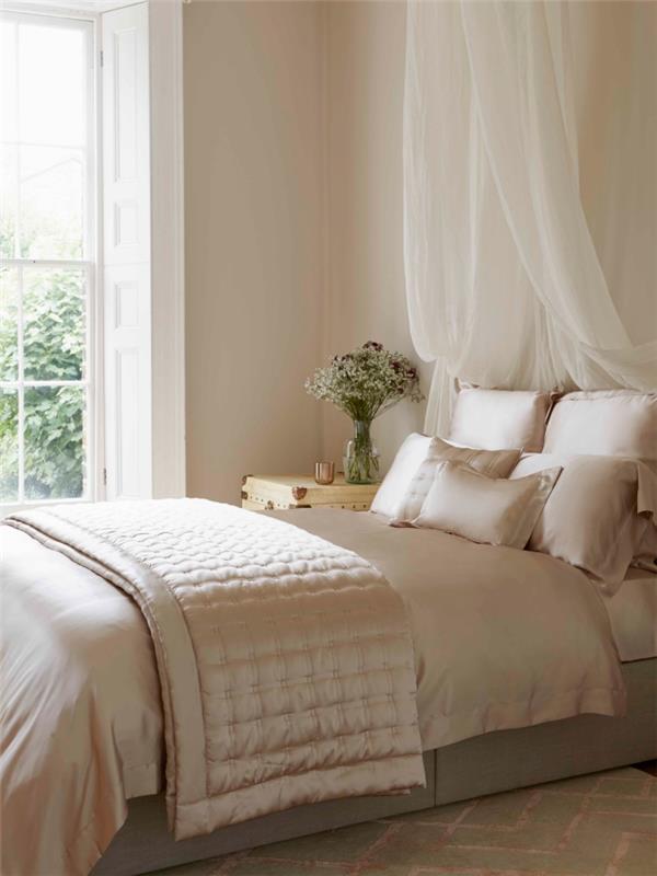 bej duvarlar ve gölgelik yatak ve hafif ahşap komodin ile beyaz pencere ile romantik yatak odası için renk