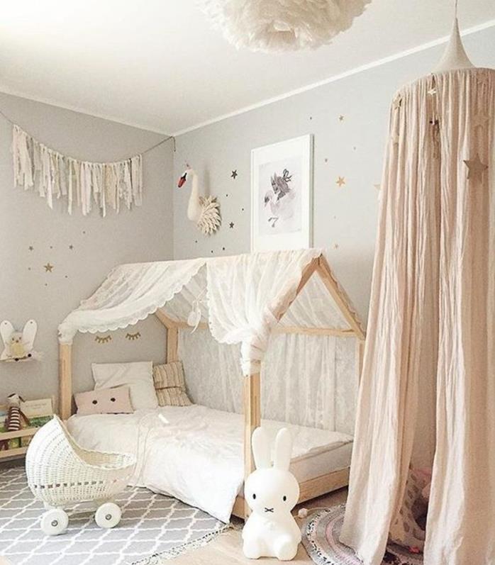 „Montessori“ kūdikio lovytė, pilkas kilimas su baltais raštais, lova masonete, balta patalynė, pilka siena, zuikio žaislas, pilka siena, baltos lubos, vaikiškas triukas