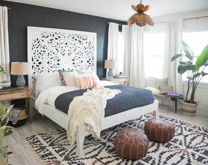 balta lova, tradicinis kilimas, odinės kėdės, didelis žalias augalas, du mediniai naktiniai staleliai