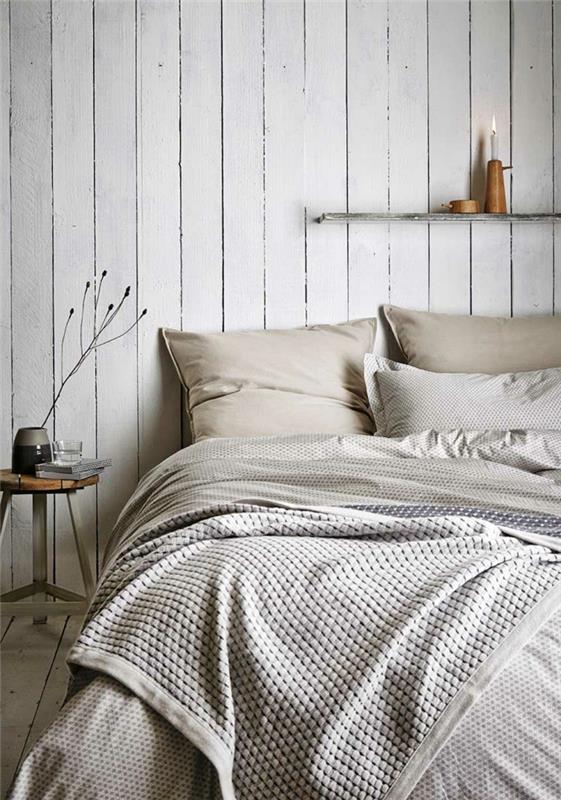 šviesiai pilkas miegamasis, medinė kėdė, sieninė lentyna su medine žvakidė, geometrinis antklodės užvalkalas