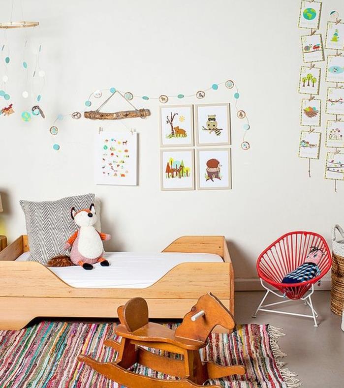 balta dažų spalva, medinės lirtos ant grindų, baltas čiužinys, žaislas iš lapės, supamoji kėdė, įvairiaspalvis kilimas, sienų dekoravimo dizainas, Montessori metodas vaikų miegamasis