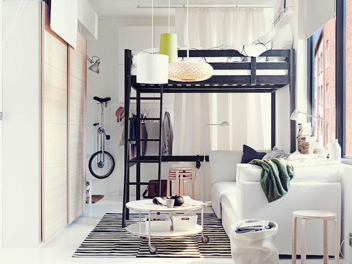 juoda aukšta lova, balta sofa ir apvalus kavos staliukas su ratukais ant zebros kilimo, baltos sienos, užuolaidos langui uždengti, spinta su medinėmis stumdomomis durimis