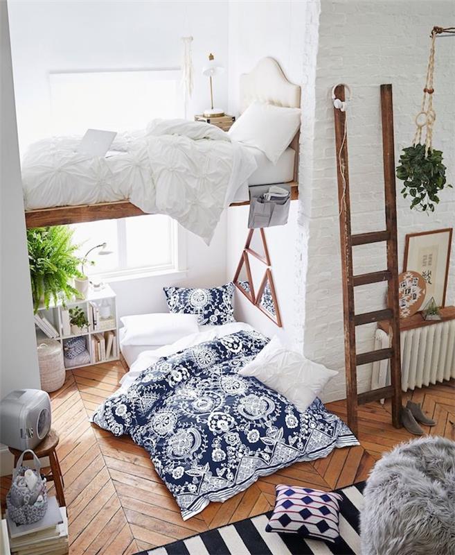 mažas buto išplanavimas su aukšta medine lova, medinėmis parketo grindimis su čiužiniu ir mėlyna bei balta patalyne, kaimiškomis medinėmis kopėčiomis