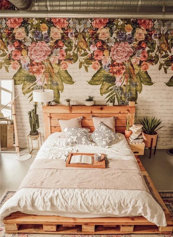 paletna postelja z vzglavnikom iz lesa, naredi sam, stena okrašena s cvetličnim tiskom na belih opekah, lonci z zelenimi rastlinami kot posteljna
