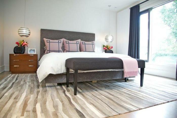 bela spalnica za odrasle barve, siva postelja in konec postelje, lesena nočna omarica, oblikovalske suspenzije, siva, bela in rjava preproga, modre zavese