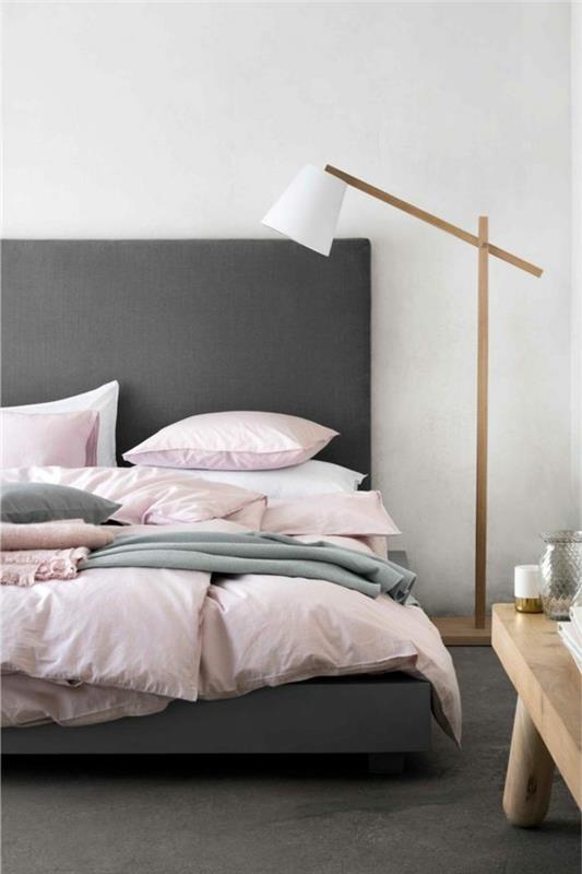postelja iz antharcita, bela, roza in svetlo siva posteljnina, temno siva preproga, lesena mizica, oblikovalska svetilka, dekor za spalnico