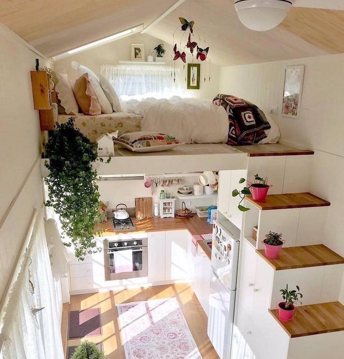 lova antrame aukšte, į kurį laiptai veda į autobusą, miegamoji zona po šlaitu, kompaktiška virtuvė iš medžio ir baltos spalvos