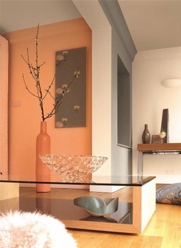 oranžinės ir baltos bei pilkos sienos, vidinis kambarys su šviesiomis laminato grindimis, svetainės spalvų idėjos, modernus stalas su stikliniu viršumi, didelė dekoratyvinė vaza ir krištolo dubuo, pilkos poilsio erdvės idėjos