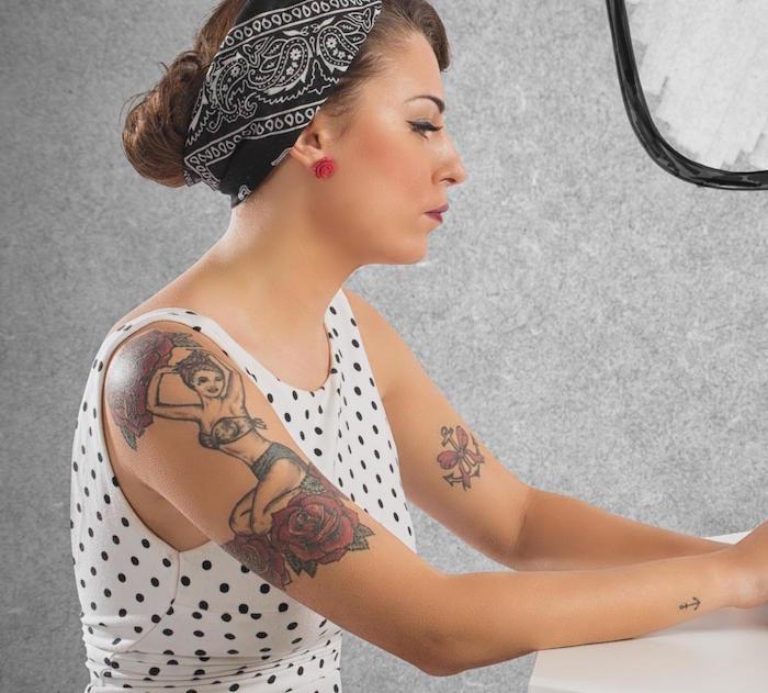 tetovaža z roko za žensko s 50 -letnim pin up videzom s polka pik obleko in črno bandano v laseh in vozlom sidro tetovaža na rokavu