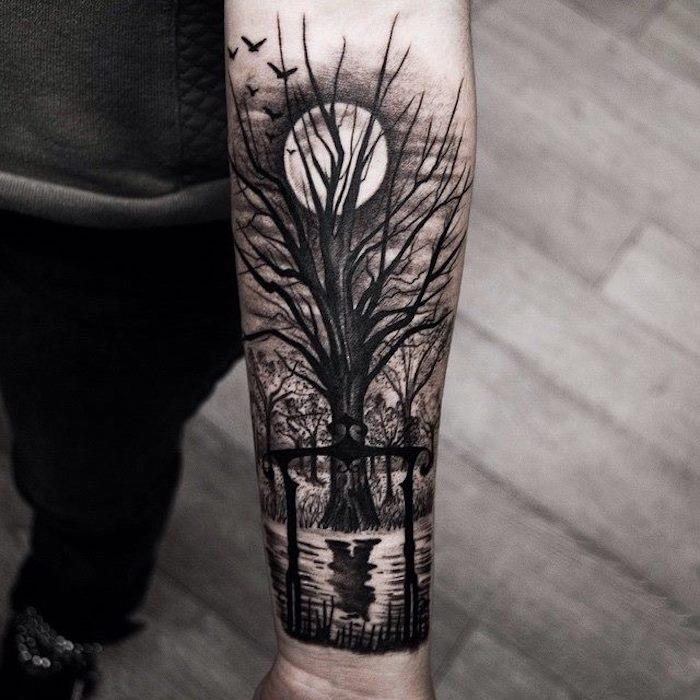 Tatuaggi sulla spalla uomo con il disegno di una foreta al tramonto con albero e lago