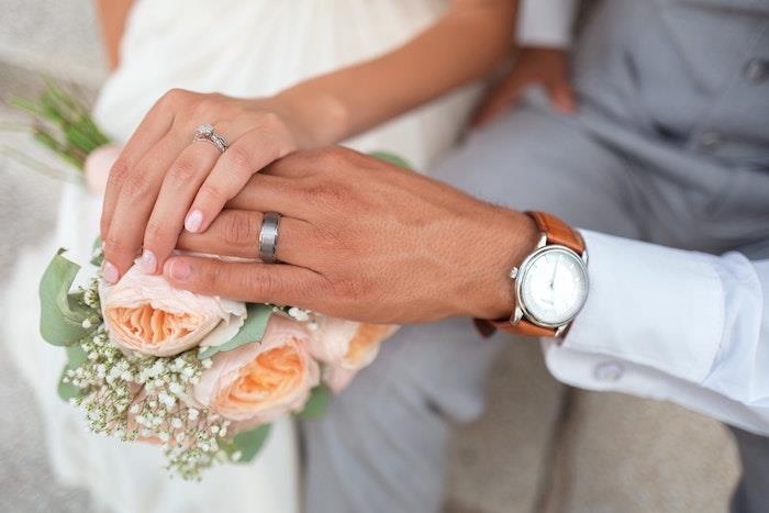 Z roko v roki dva klasična platinasta poročna prstana, poročni šopek za žensko in moškega