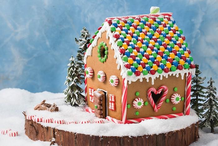 küçük bir evin çatısını süslemek için mm şekerler, küçük kurabiyeler, dev şeker şekerleri, ahşap bir kütük üzerinde gurme dekoratif kompozisyon