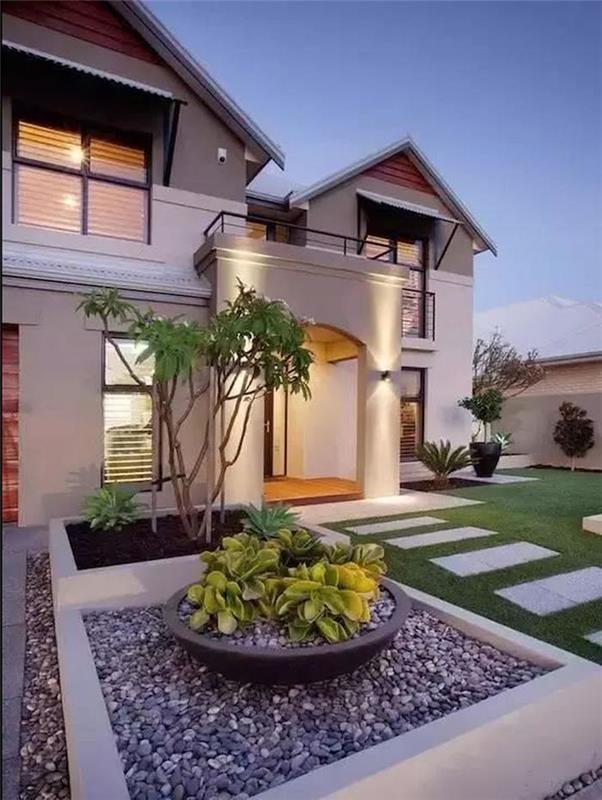 Önünde çimenlik olan ve çakıl taşlarıyla dolu dekoratif bir kareye sahip ultra modern ev