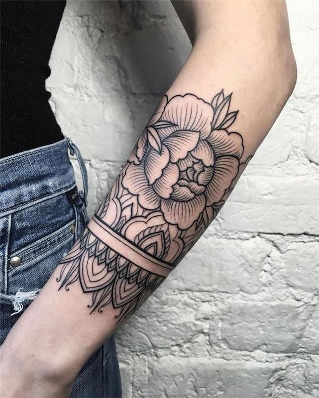 tetovaža roke, vzorec potonike, bela opečna stena, modre kavbojke, črni top, tetovaža cvetja in mandale