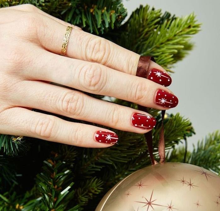 Božična manikura v rdeči barvi z belimi pikami in belimi zvezdicami, zlato božično kroglico in borovimi vejami