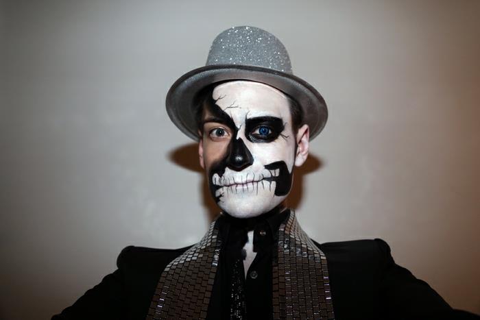 kaukolės makiažas, žvilganti pilka skrybėlė, juodas kostiumas, juodos ir baltos pusės kaukolės makiažas