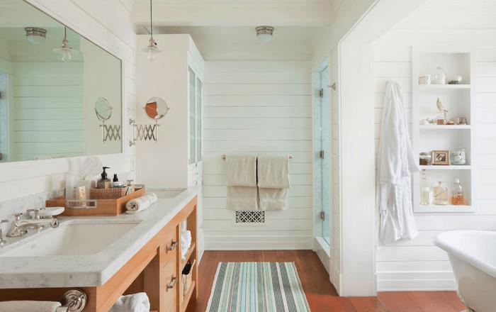 Velika omara, bele police za shranjevanje v steni, ločena kad in tuš, modra, zelena in siva kopalniška preproga in lesena omarica z rožnatim podtonom