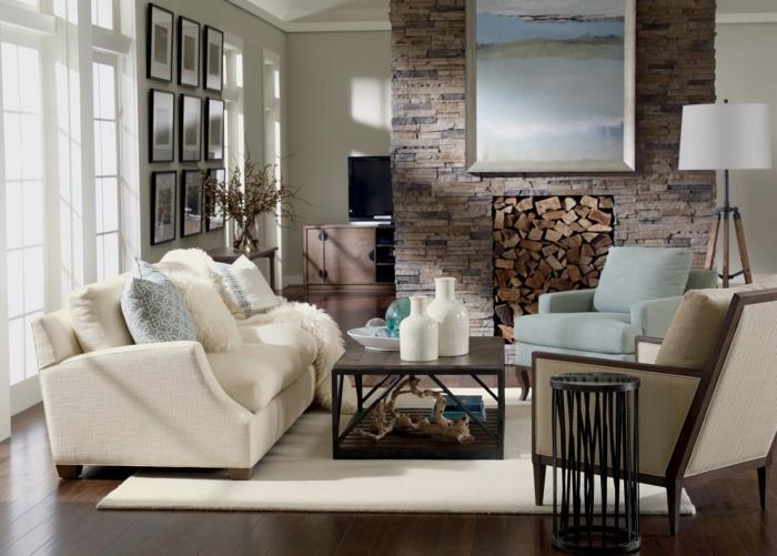 prašmatnus ir kaimiškas kaimo dekoras, rudas parketas, balta sofa, medinis kavos staliukas, akmeninis židinys, pilkas ir mėlynas fotelis, baltas kilimas