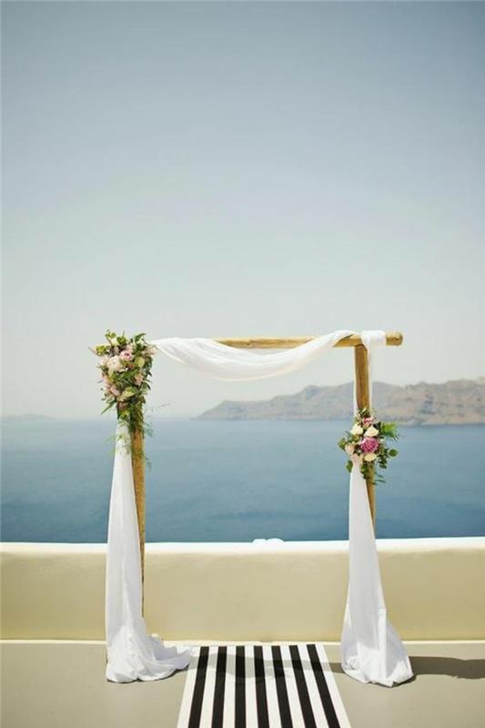 vestuvės-graikija-ceremonija po atviru dangumi-vestuvių arka-tiulis ir gėlių puokštės