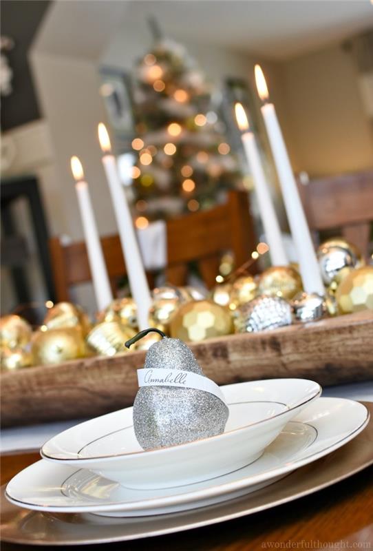 beyaz tabakta parıldayan armutta yer kartı, altın ve gümüş Noel süsleri ve beyaz mumlar ile ahşap merkez